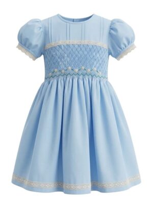 Vestido infantil azul con mangas abultadas, detalles de encaje en mangas y ruedo, y cuerpo smock bordado con motivos florales. Diseño clásico y artesanal, ideal para ocasiones especiales.